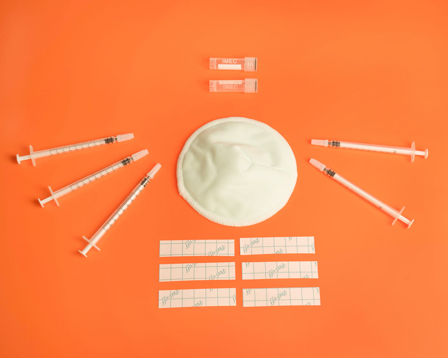 5 colostrum syringes, one reusable breastpad, two storage pots and stickers, on an orange background.